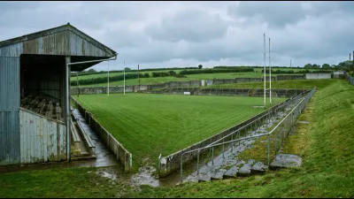 A large county sports ground with a single covered stand and open grass banking on the far side, under soft grey Irish light