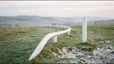 The white running rail of a turf racecourse curving across close-cropped downland grass, rolling open downs falling away out of focus behind