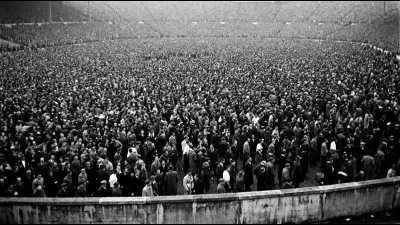 Illustration in the style of a mid-century press photograph: a vast packed open standing terrace of spectators in black and white, faces indistinct. Not an archive image
