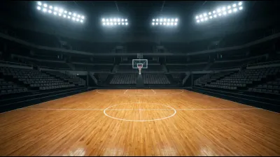 An empty indoor basketball arena with polished hardwood floor and tiered seating, lit by overhead spotlights from above the court