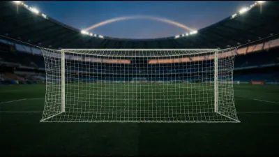 An empty football goal with plain white netting on stadium turf at dusk, the tiers of a vast empty national stadium out of focus behind it