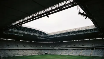 The interior of a large empty stadium seen from the lower tier, its retractable roof half open with a bright slot of overcast sky above rows of grey seats
